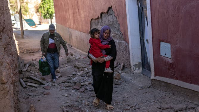 A woman carries a child over rubble from damaged buildings following yesterday's earthquake, on September 10, 2023 in Moulay Brahim, Morocco.